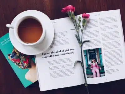 opened book with pink flower on top near filled ceramic mug